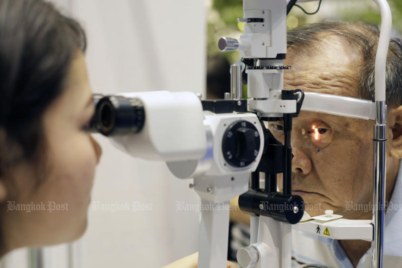 An optometrist examines the eyes of an elderly man at the Queen Sirikit National Convention Center (QSNCC) in Bangkok. (Photo: Pornprom Satrabhaya)