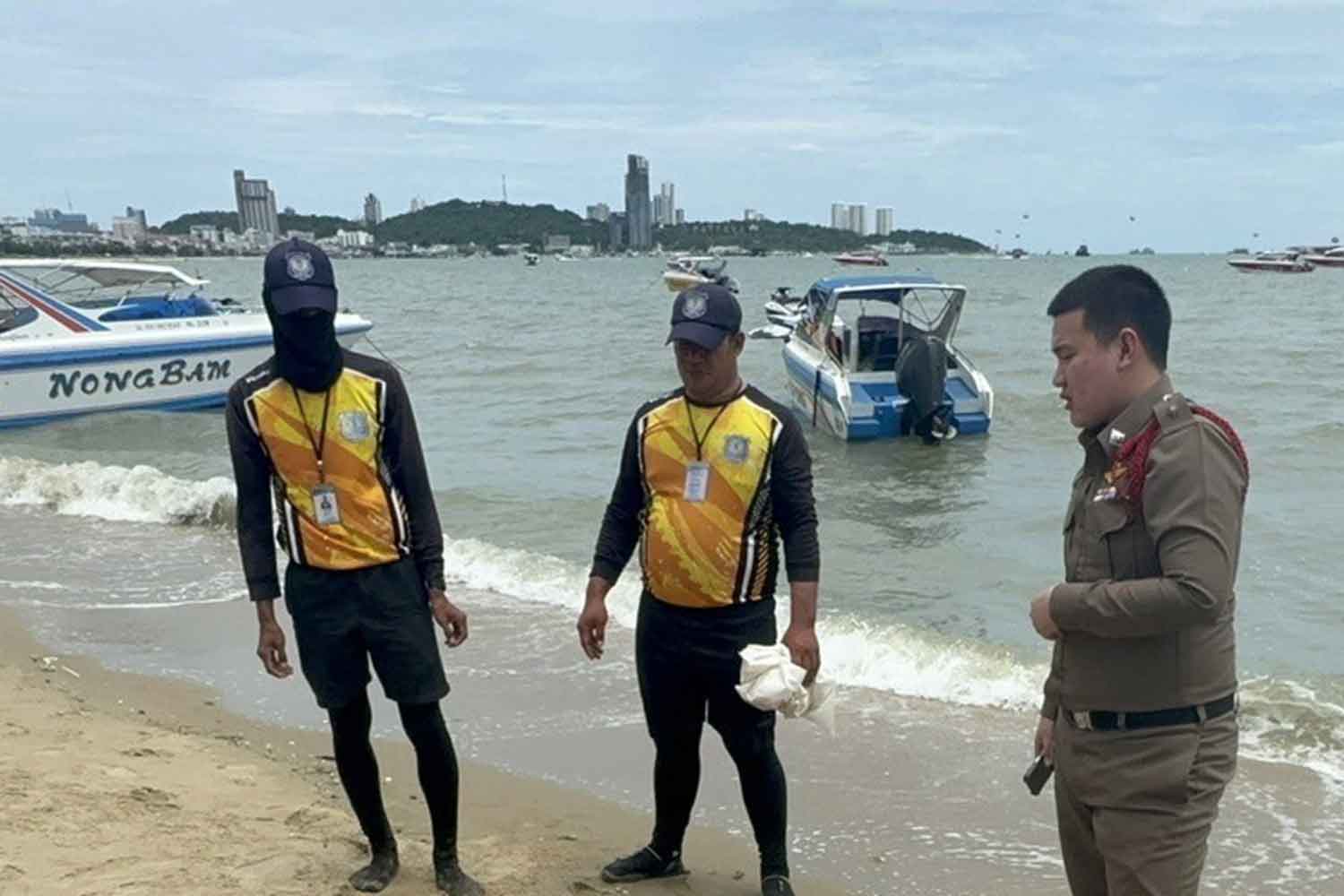 A policeman and lifeguards look at the body on Pattaya beach on Sunday. (Photo: Chaiyot Pupattanapong)